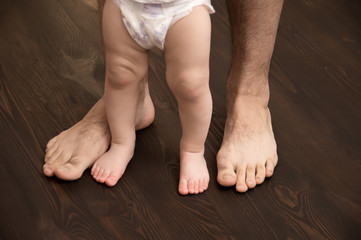 The child makes the first step. Large male legs with small baby legs. Dad helps the child take the first steps.
