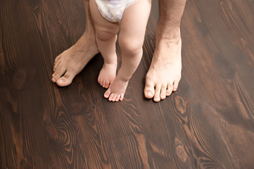The child makes the first step. Large male legs with small baby legs. Dad helps the child take the first steps.
