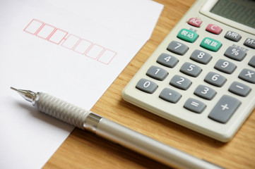 木製のデスクの上に置かれた白い封筒とペンと電卓