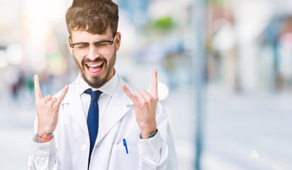 Young professional scientist man wearing white coat over isolated background shouting with crazy expression doing rock symbol with hands up. Music star. Heavy concept.