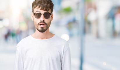 Young handsome man wearing sunglasses over isolated background afraid and shocked with surprise expression, fear and excited face.