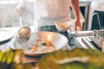 Chef takes out with slotted spoon hot steaming egg noodles from pan