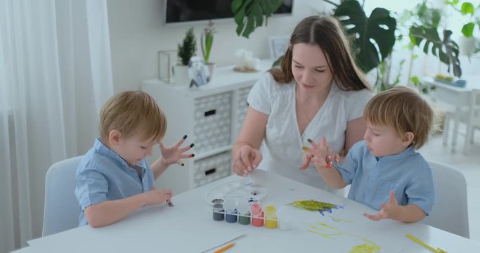 Two children of boys and mother are engaged in creative development doing homework by fingering on paper. The development of tactile sensations and small mathematics.