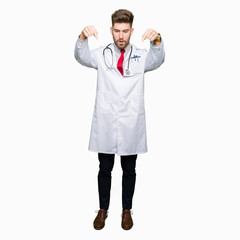 Young handsome doctor man wearing medical coat Pointing down with fingers showing advertisement, surprised face and open mouth