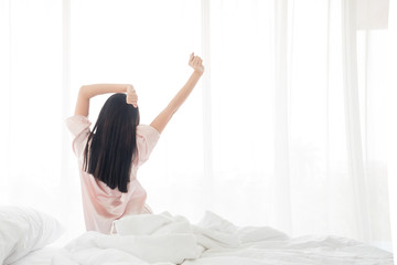 Woman in bed stretching body after waking up in the morning, back view sitting near the white window and getting ready for a new day ,Copyspace