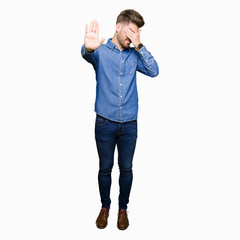 Fototapeta premium Young handsome blond man wearing casual denim shirt covering eyes with hands and doing stop gesture with sad and fear expression. Embarrassed and negative concept.
