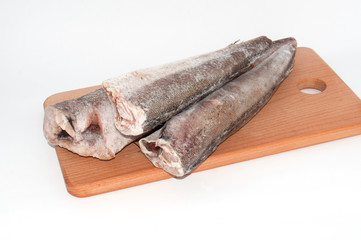 Frozen fish hake close-up on a wooden cutting board on a white background close-up