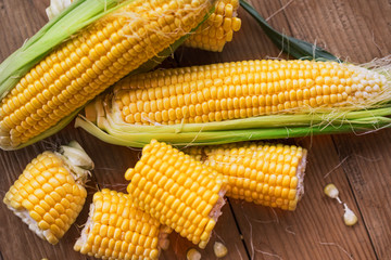 Fresh corn on cobs on rustic wooden table, closeup. Ripe corn. Half of broken open sweet corn