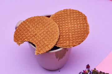Stroopwafel placed on top of the cup of hot coffee or tea served on pink background