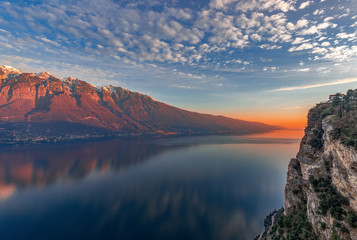 Stunning sunset on Lake Garda. View of the snowy Alps painted by the setting sun from the cliff of the city Tremosine. Winter period. Lombardy, Italy - obrazy, fototapety, plakaty