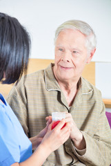 Asian nurse giving pills to aged senior man in hospital