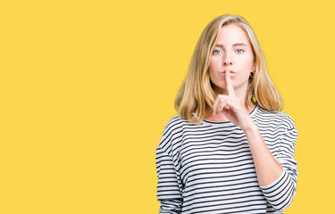 Beautiful young woman wearing stripes sweater over isolated background asking to be quiet with finger on lips. Silence and secret concept.