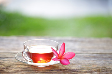 Red tea in clear glass and flower background on wooden table
