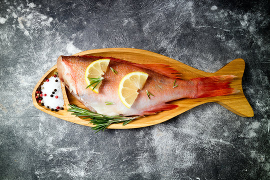 Fish raw snapper with lemon slices, herbs rosemary, salt and pepper on dark background. Healthy food and dieting concept. Top view, copy space