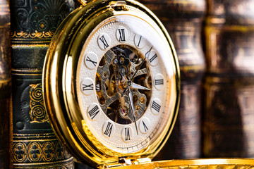 Antique clock on the background of vintage books. Mechanical clockwork on a chain.