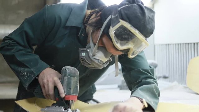 profession, people, carpentry, emotion and people concept -A carpenter cuts a board with an electric jigsaw. manufacture of skateboards. he has protective clothing and mask. 4k