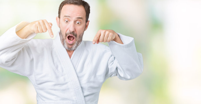 Handsome middle age senior man wearing kimono uniform over isolated background Pointing down with fingers showing advertisement, surprised face and open mouth