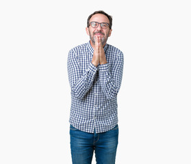 Handsome middle age elegant senior man wearing glasses over isolated background praying with hands together asking for forgiveness smiling confident.