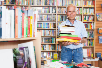 Elderly male holding stack of books in bookshop interior