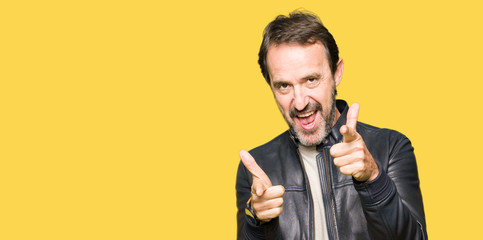Middle age handsome man wearing black leather jacket pointing fingers to camera with happy and funny face. Good energy and vibes.
