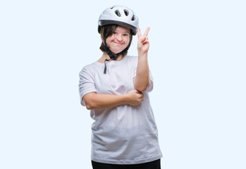 Young adult cyclist woman with down syndrome wearing safety helmet over isolated background smiling with happy face winking at the camera doing victory sign. Number two.
