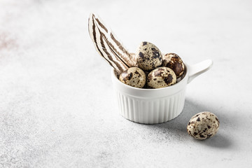 Close up quail eggs with bird feather in the white ceramic bowl on the white background