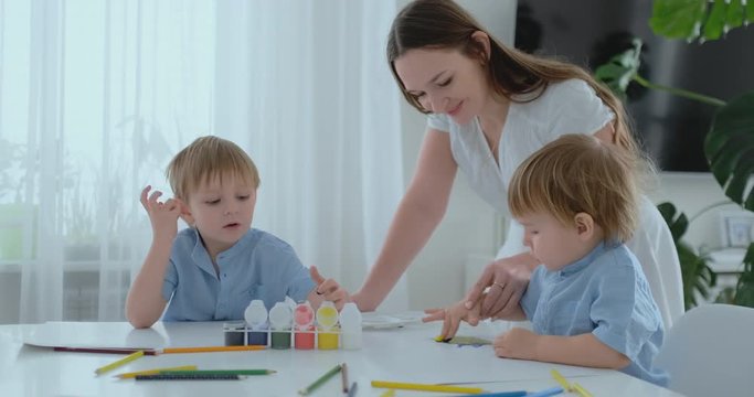Mom helps her sons to develop creative skills and is engaged with them to create drawing paints with the help of fingers. Child development. Creative family. Loving mom