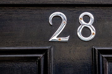 House number 28 with the twenty eight in embossed shiny silver on a black house door