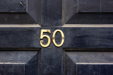 House number 50 with the fifty in bronze numbers screwed to a black wooden house door