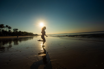 Fototapeta premium Woman runs barefoot on the beach at sunset. Silhouette of a woman by the sea at sunrise