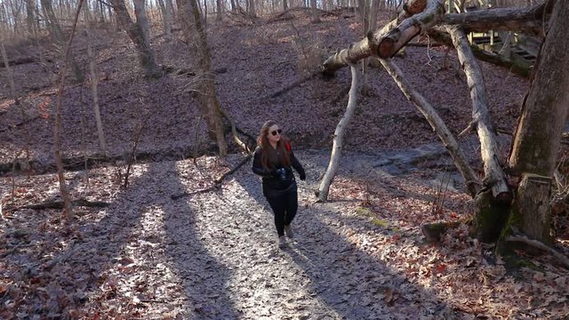 A girl photographer is exploring a forest trail. She carries a DSLR strapped around her neck.