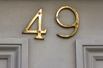 House number forty-nine with the 49 in shiny bronze metal numbers screwed onto the creme door with...