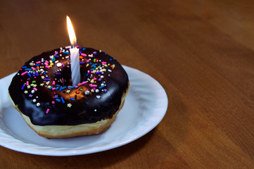 Chocolate dipped donut with sprinkles with birthday candle 