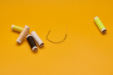 coils of thread with needles on yellow background
