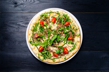 Fresh arugula and tomato pizza on black table