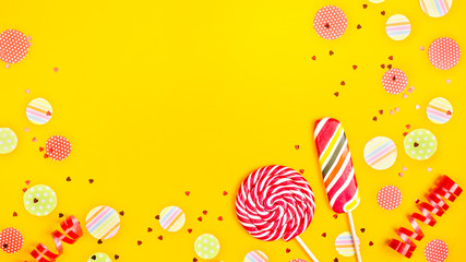 Two multicolored candies among paper circles of confetti, glitter and festive ribbons on a bright...