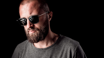 Obraz premium Portrait of a handsome balded man with long well trimmed beard wearing sunglasses and grey shirt.