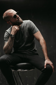 Portrait of a handsome balded man with long well trimmed beard wearing sunglasses and grey shirt looking away to side.