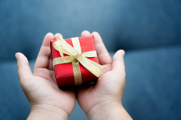 Close up of a hand holding a red gift box tied with a gold ribbon. It is a joy to celebrate the holidays, such as Valentine's Day, Christmas and Happy New Year. Concept Universal Children’s Day