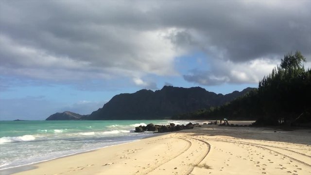 Pan of Bellows Beach in Oahu, Hawaii. Man stands with Boogie board ready to hit the water.