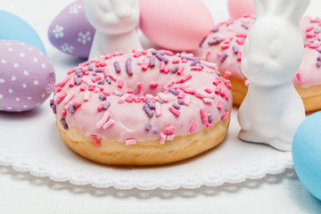 stylish easter donuts and painted eggs on rustic wooden background top view with candle yellow flowers