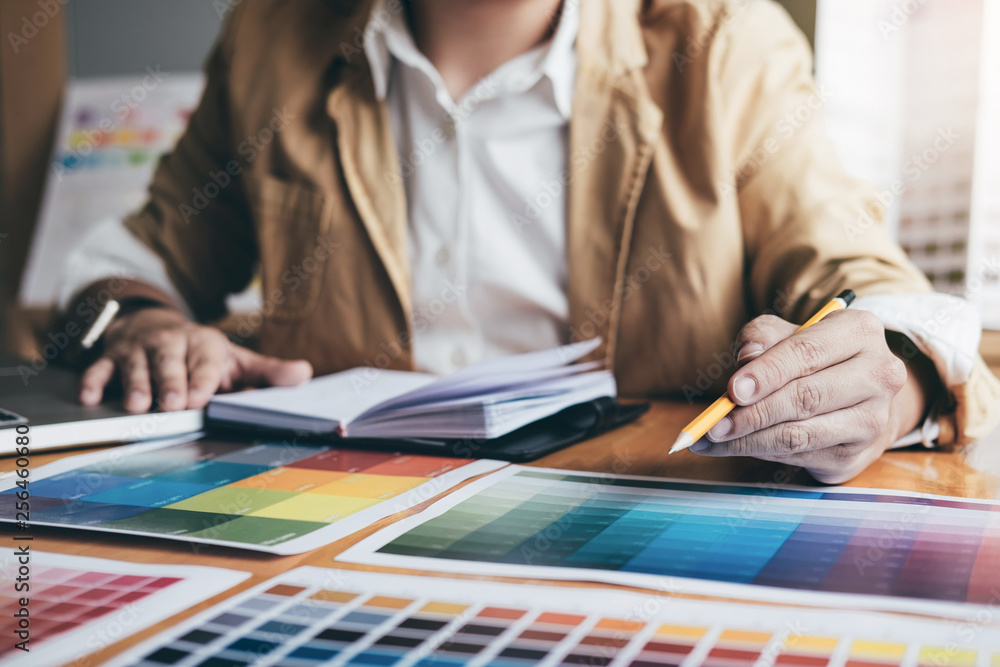 Poster Young creative Graphic designer using graphics tablet to choosing Color swatch samples chart for selection coloring with work tools and accessories at workplace