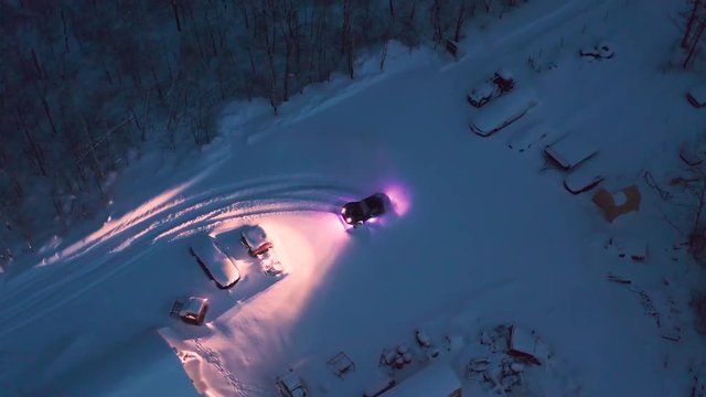 A birds eye view of a custom built off road miata car doing some donuts in a fresh snowy parking lot.