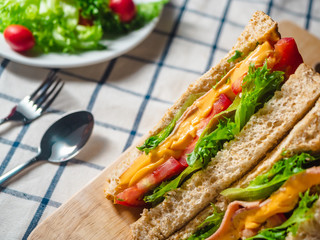 Close up of Sandwich with ham, cheese, tomatoes, lettuce, and toasted bread on the  wooden cutting board.