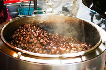 Chestnuts are being roasted in a traditional roasted pot, with smoke rising above.