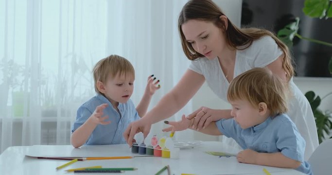 Mom helps her sons to develop creative skills and is engaged with them to create drawing paints with the help of fingers. Child development. Creative family. Loving mom