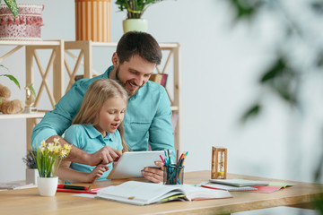 Father and his daughter are smiling while spending time together. A day with family. Young pretty girl and her dad are studying with tablet. Education, studying and knowledge sharing concept.