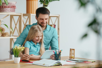 Father and his daughter are smiling while spending time together. A day with family. Young pretty girl and her dad are studying with tablet. Education, studying and knowledge sharing concept.