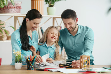 Fototapeta premium Father, mother and their daughter are smiling while spending time together. A day with family. Young happy couple with child are studying with the book. Education, studying and knowledge sharing