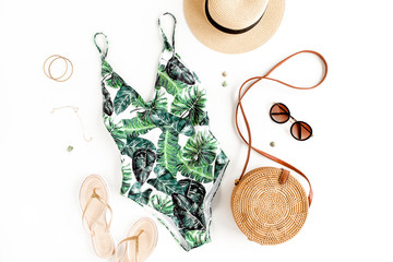 Woman's beach accessories: swimsuit with tropical print, rattan bag, straw hat on white background....